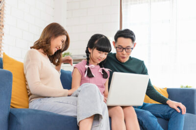 Happy Asian Family Using Laptop Sitting On A Couch 