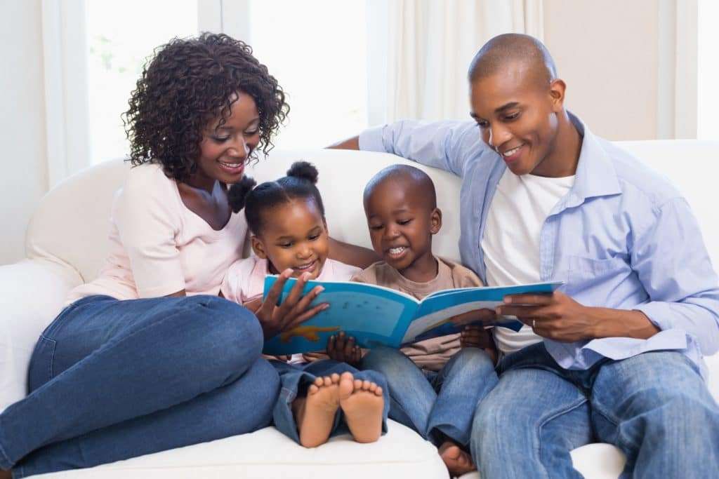 Happy Family Sitting On The Couch Reading A Story Book